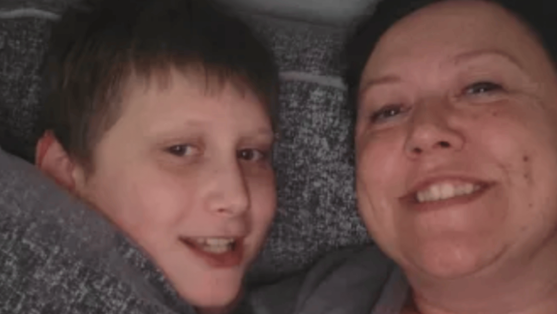 Lady laying down with a boy, both are smiling at the camera.