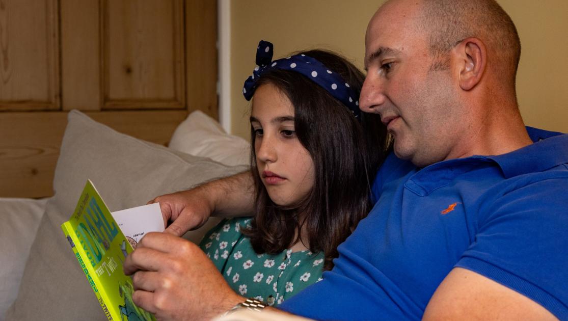 Man sat reading a book with his daughter
