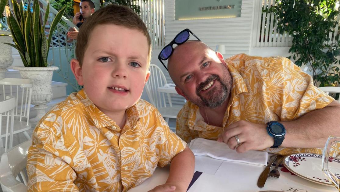 Man & child sat a table wearing matching shirts.