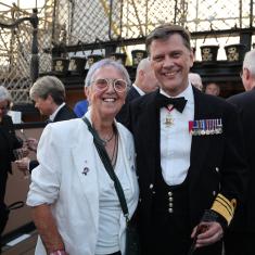 A man and woman stand on the deck of HMS Victory. The man is dressed in official Royal Navy DRESS ATTIRE.