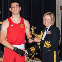 Boxer in red being presented with an award from a Royal Navy Officer