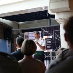 person speaking on stage presenting to a naval audience