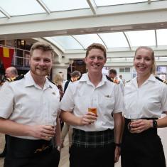 three naval personnel, two men, one oman, smiling at the camera and holdng drinks