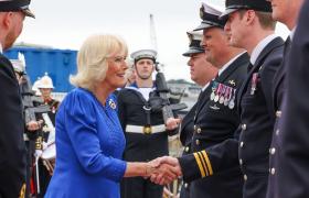 The Queen wearing a royal blue dress is greeting service personnel dressed in uniform at the HMS Astute homecoming and garden party. 