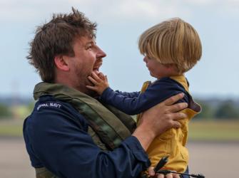 Man from the Naval Air Squadron holding a child in his arms. 