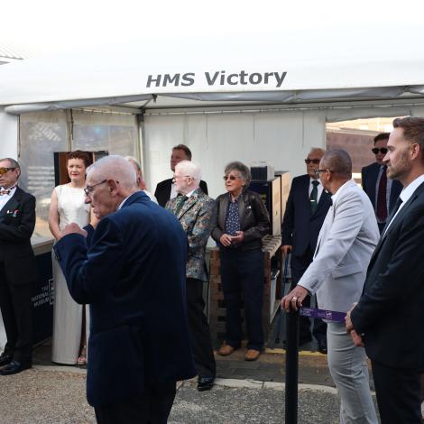 People waiting outside the HMS Victory in formal dress attire.