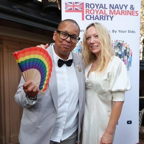 a couple standing in forn of an RNRMC banner, one is holdnig a rainbow fan.