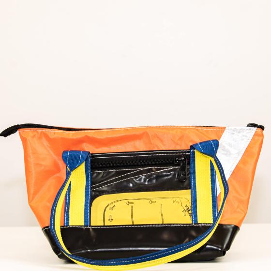 Left side of bag. Black and Orange with black zipped pocket and life raft feature. 