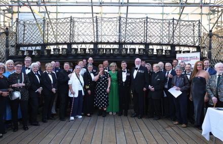 Group of people posing for a photo at a formal dining out event on the deck of the HMS Victory. 