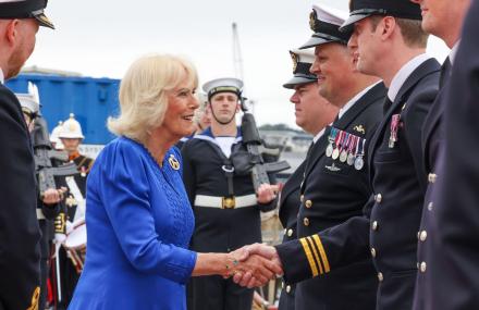The Queen wearing a royal blue dress is greeting service personnel dressed in uniform at the HMS Astute homecoming and garden party. 