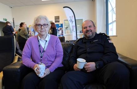 Lady sat with a gentleman in a naval outfit. They are sat on a sofa with mugs. 