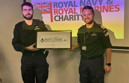 Two men standing infront of an RMRNC screen - one is holding a picture of a boat. Both are smiling at the camera.