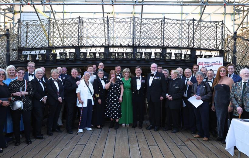 Group of people posing for a photo at a formal dining out event on the deck of the HMS Victory. 