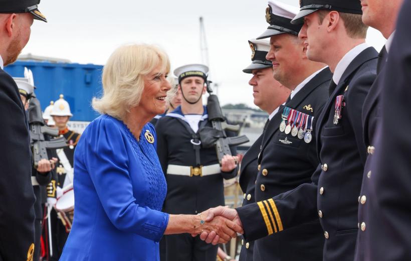 The Queen wearing a royal blue dress is greeting service personnel dressed in uniform at the HMS Astute homecoming and garden party. 